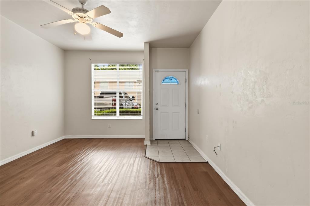 An empty room with wood-look flooring, a ceiling fan, a window, and a front door — 4415 SW 34TH STREET UNIT 309, GAINESVILLE, FL