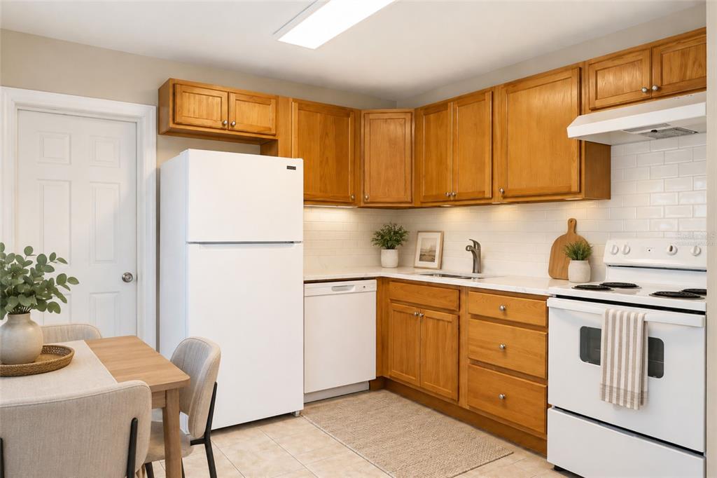 A kitchen features wood cabinets, white appliances, a tiled backsplash, and a small dining area — 9412 N ELMER STREET, TAMPA, FL