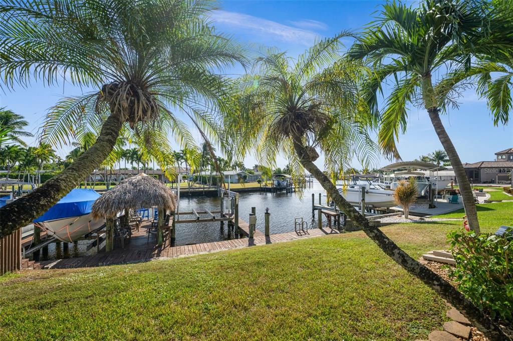 A grassy backyard overlooks a canal with a boat dock, tiki hut, and palm trees — 4803 SW SANTA BARBARA COURT UNIT 8, CAPE CORAL, FL