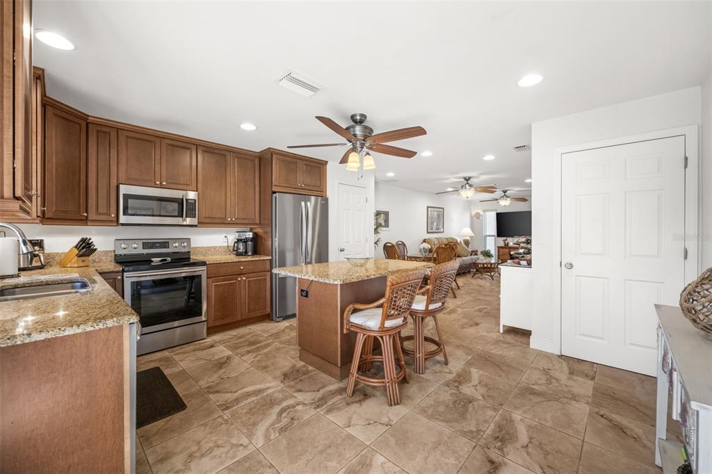 A kitchen with wood cabinets, granite countertops, and a center island opens to a living area — 4803 SW SANTA BARBARA COURT UNIT 8, CAPE CORAL, FL