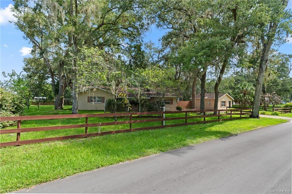 A single-story house with a brown roof sits behind a wooden fence and large trees — 4929 E SHADY ACRES DRIVE, INVERNESS, FL