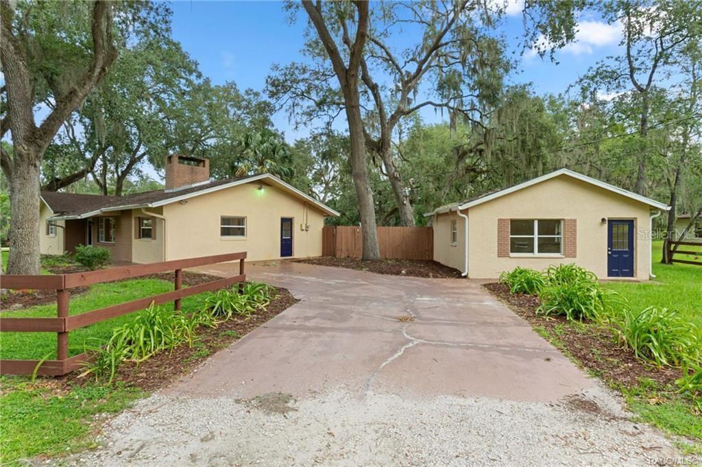 A concrete driveway leads to a house and a detached garage under large oak trees — 4929 E SHADY ACRES DRIVE, INVERNESS, FL