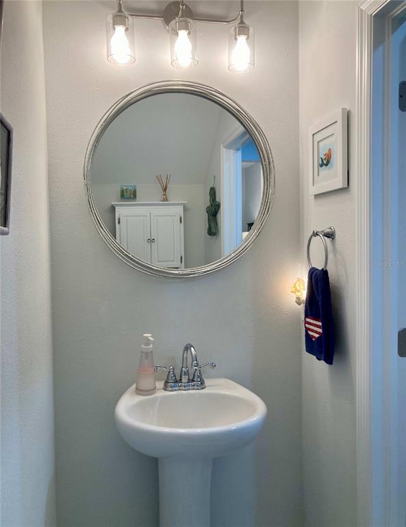 A bathroom features a pedestal sink, a round silver-framed mirror, and a three-light vanity fixture — 10824 QUICKWATER COURT, RIVERVIEW, FL