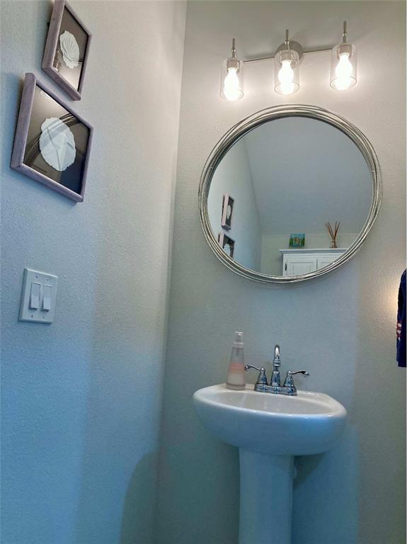 A small bathroom features a pedestal sink, a round mirror, and two framed wall decorations — 10824 QUICKWATER COURT, RIVERVIEW, FL