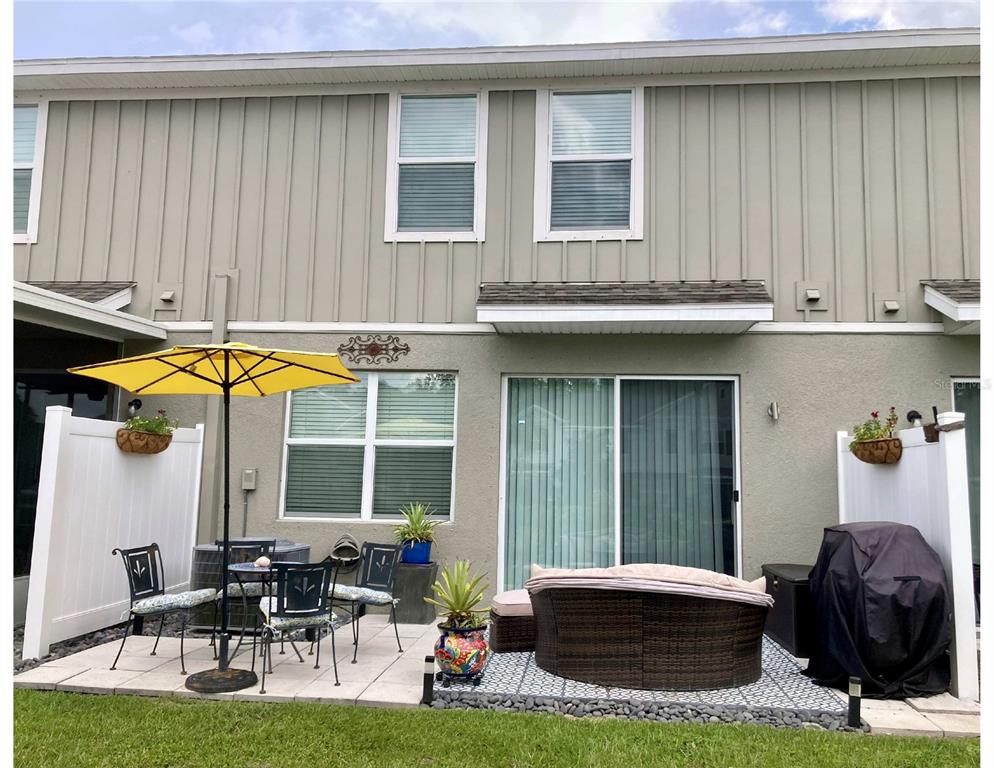 A patio with a yellow umbrella, outdoor furniture, and a grill sits behind a townhouse — 10824 QUICKWATER COURT, RIVERVIEW, FL