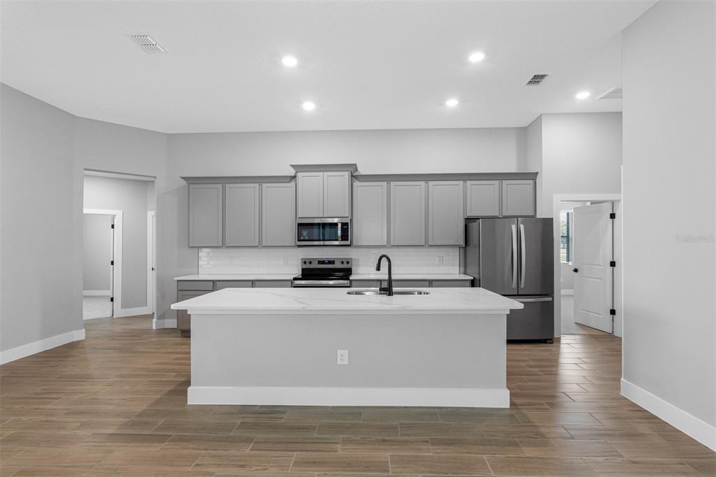 A modern kitchen features gray cabinets, a white marble island, and light wood-look tile flooring — 13509 WALDEN SHEFFIELD ROAD, DOVER, FL