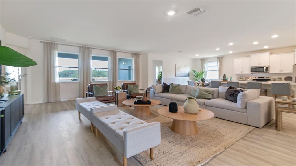 An open-concept living room features a sectional sofa, two coffee tables, and a kitchen area — 3064 KINGSMAN TRAIL, ORMOND BEACH, FL