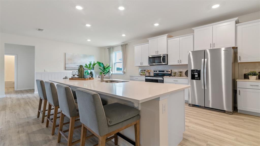 A modern kitchen features a large white island, stainless steel appliances, and light wood flooring — 3064 KINGSMAN TRAIL, ORMOND BEACH, FL