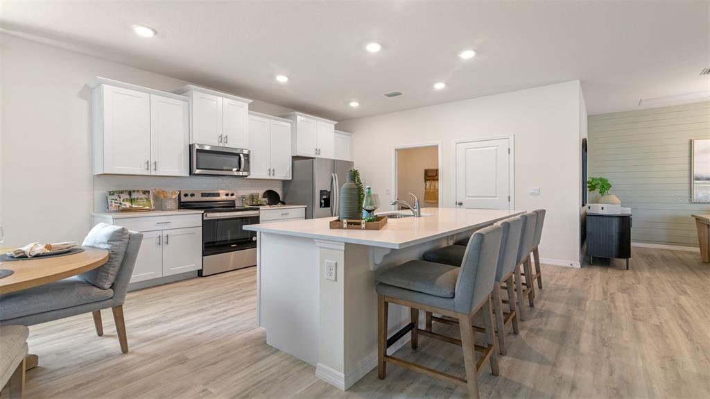 A modern kitchen features white cabinets, a large island with bar seating, and light flooring — 3064 KINGSMAN TRAIL, ORMOND BEACH, FL