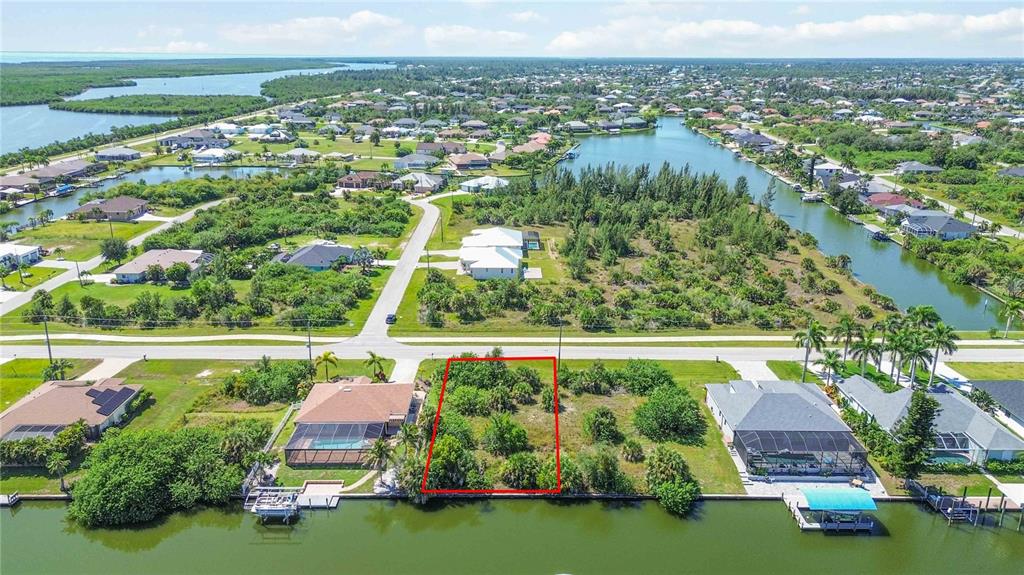 An aerial view shows a vacant waterfront lot outlined in red between two residential houses — 8633 CALUMET BOULEVARD, PORT CHARLOTTE, FL