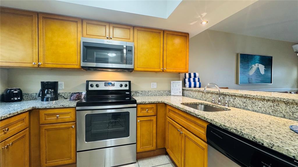 A kitchen features wooden cabinets, granite countertops, stainless steel appliances, and a double sink — 1124 SPACEPORT COURT, KISSIMMEE, FL