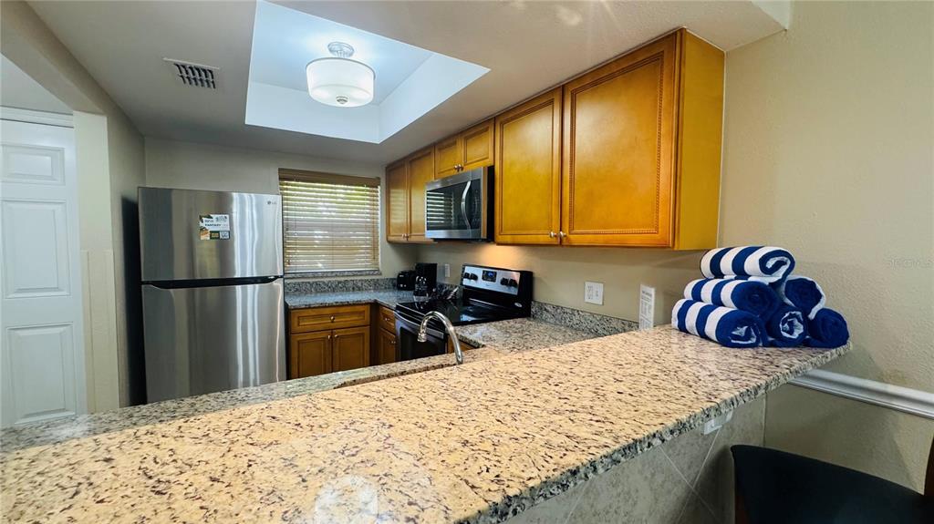 A kitchen features granite countertops, wood cabinets, stainless steel appliances, and a recessed ceiling light — 1124 SPACEPORT COURT, KISSIMMEE, FL