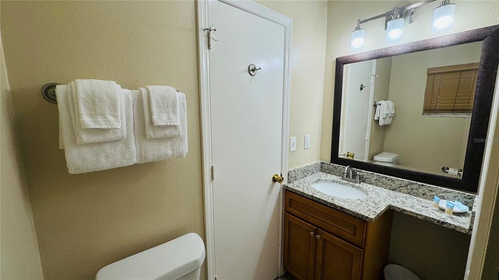 A bathroom features a granite vanity, a framed mirror, and white towels on a wall rack — 1124 SPACEPORT COURT, KISSIMMEE, FL