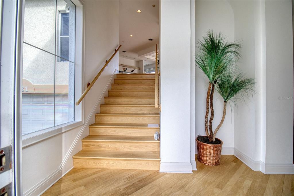 A wooden staircase leads upward from a foyer with light wood flooring and a potted plant — 131 SANDS POINT DRIVE, TIERRA VERDE, FL