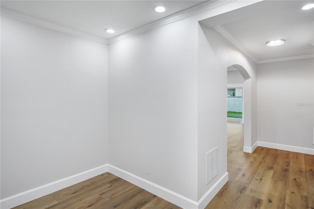 A bright room with white walls, crown molding, and wood-look flooring leads to an arched doorway — 2186 COUNTRYSIDE CIRCLE N, ORLANDO, FL