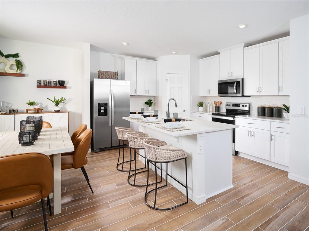 A bright kitchen features white cabinetry, a central island with bar stools, and wood-look flooring — 638 PENNYWORT STREET, LAKE ALFRED, FL
