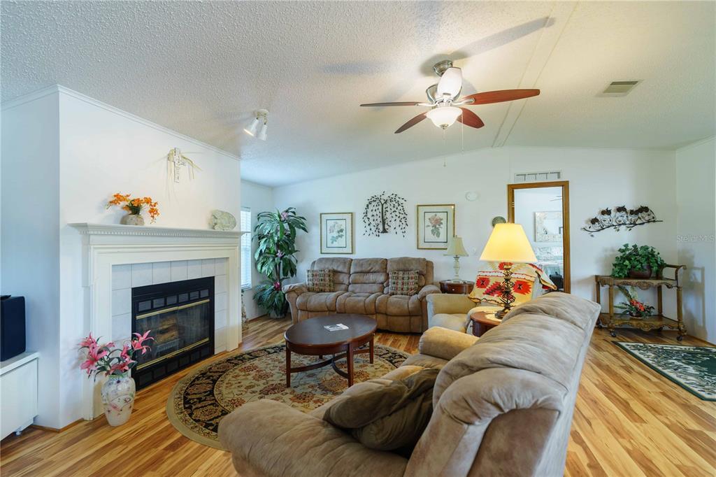 A living room features a fireplace, wood-look flooring, a ceiling fan, and two brown sofas — 13259 SE 49TH COURT, BELLEVIEW, FL
