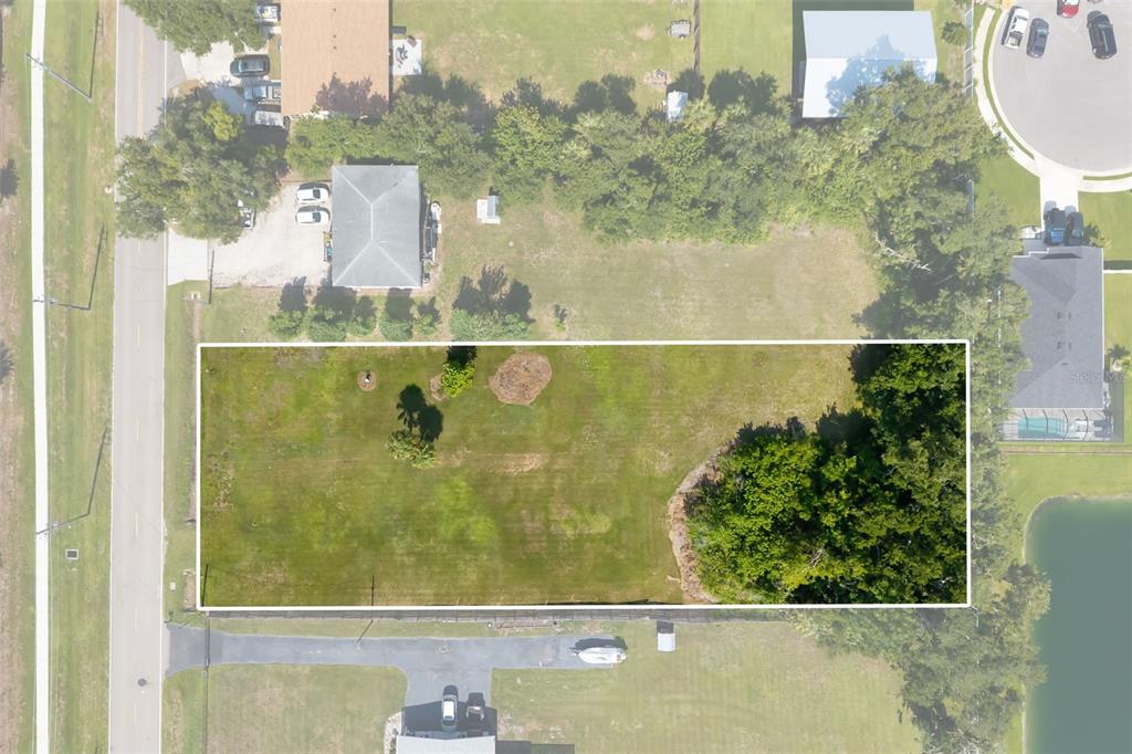 An aerial view shows a rectangular, grassy vacant lot bordered by trees and nearby houses — 2612 61ST STREET E, PALMETTO, FL