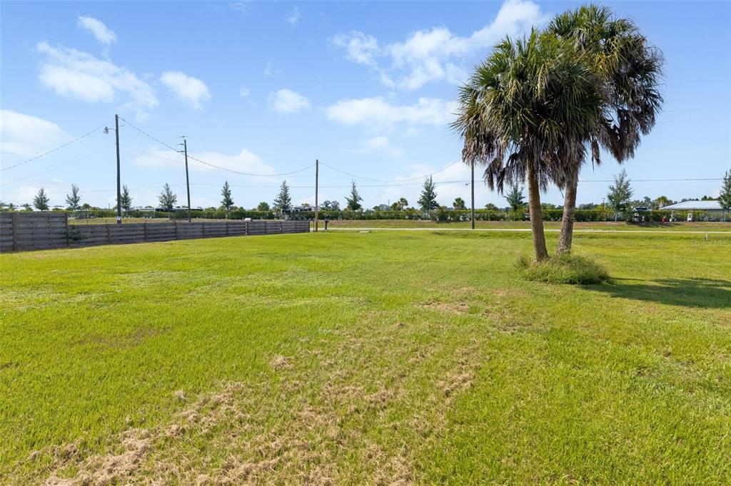 A grassy, vacant lot features a palm tree and a wooden fence under a blue sky — 2612 61ST STREET E, PALMETTO, FL