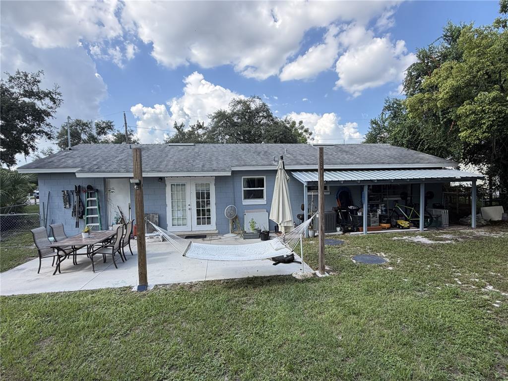 A backyard view of a gray concrete block house with a patio, hammock, and carport — 4180 POINSETTIA AVENUE, MOUNT DORA, FL