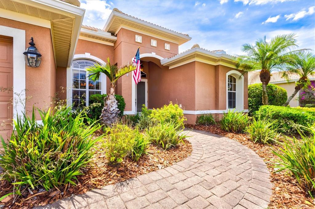 A paved walkway leads to the front entrance of a tan stucco home with landscaping — 315 PETREL TRAIL, BRADENTON, FL