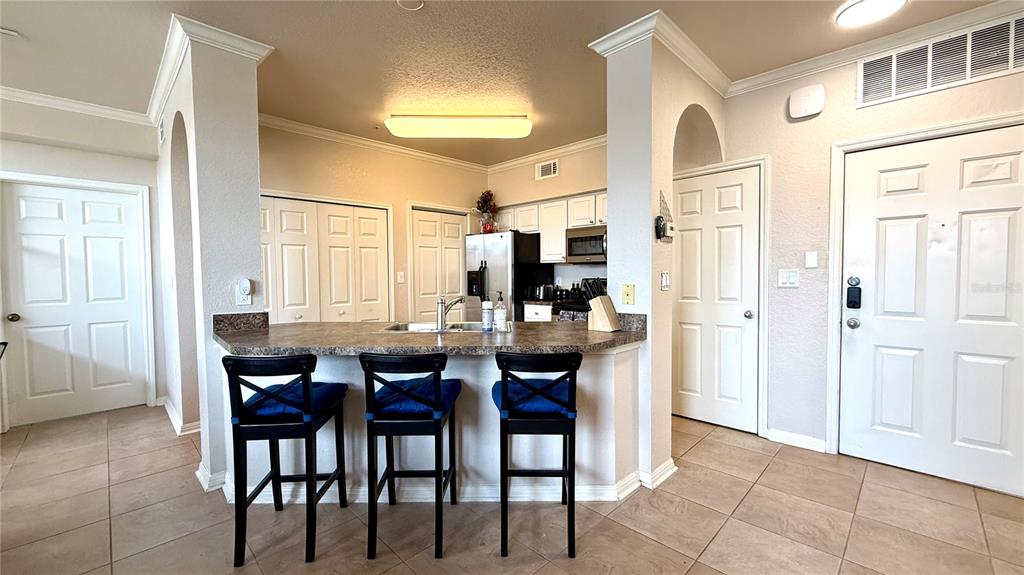 A kitchen features a breakfast bar with three stools, white cabinetry, and tile flooring — 911 N ORANGE AVENUE UNIT 243, ORLANDO, FL