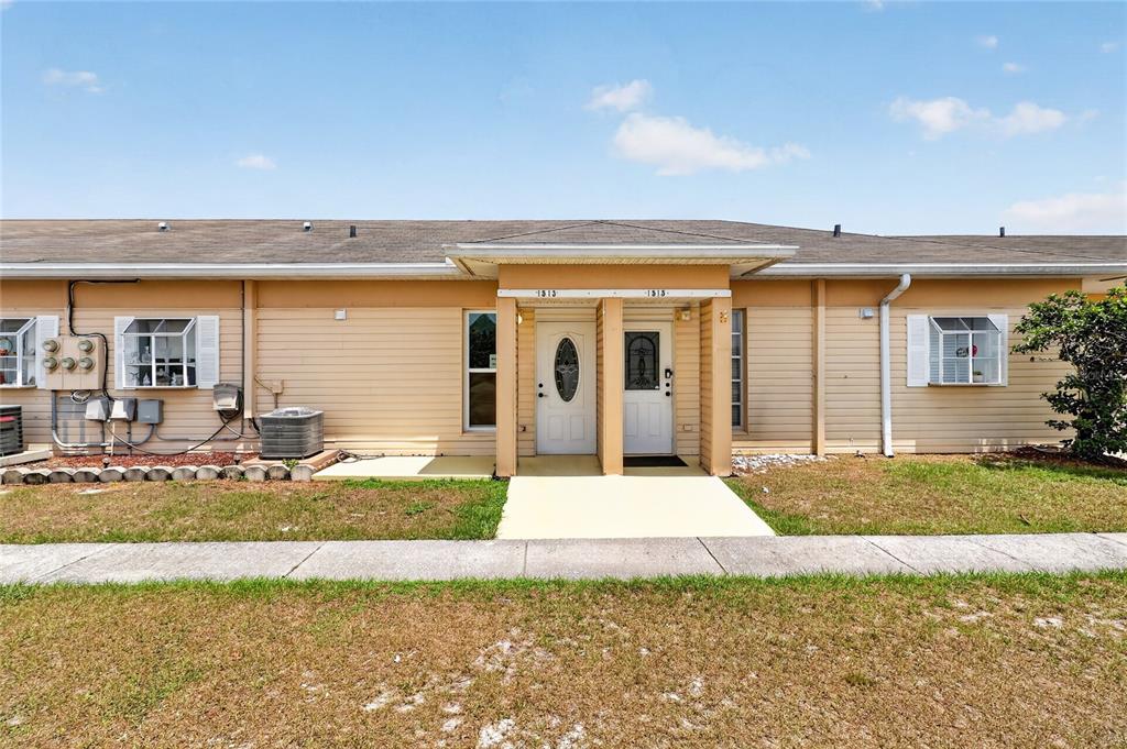 A single-story duplex with tan siding, two white front doors, and a shared covered entryway — 1513 CLUB CIRCLE UNIT 1513, LAKESHORE, FL
