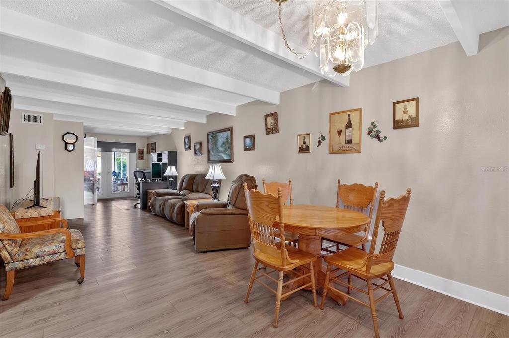 A living and dining area features wood-look flooring, white ceiling beams, and a chandelier — 1513 CLUB CIRCLE UNIT 1513, LAKESHORE, FL