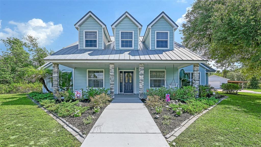 A light blue house with a metal roof and three dormers features a concrete walkway — 28401 104TH DR E, MYAKKA CITY, FL