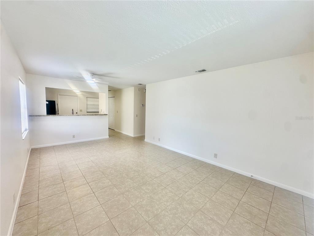 An open-concept living area features beige tile flooring, white walls, and a kitchen pass-through window — 5638 STRUTHERS COURT, WINTER HAVEN, FL