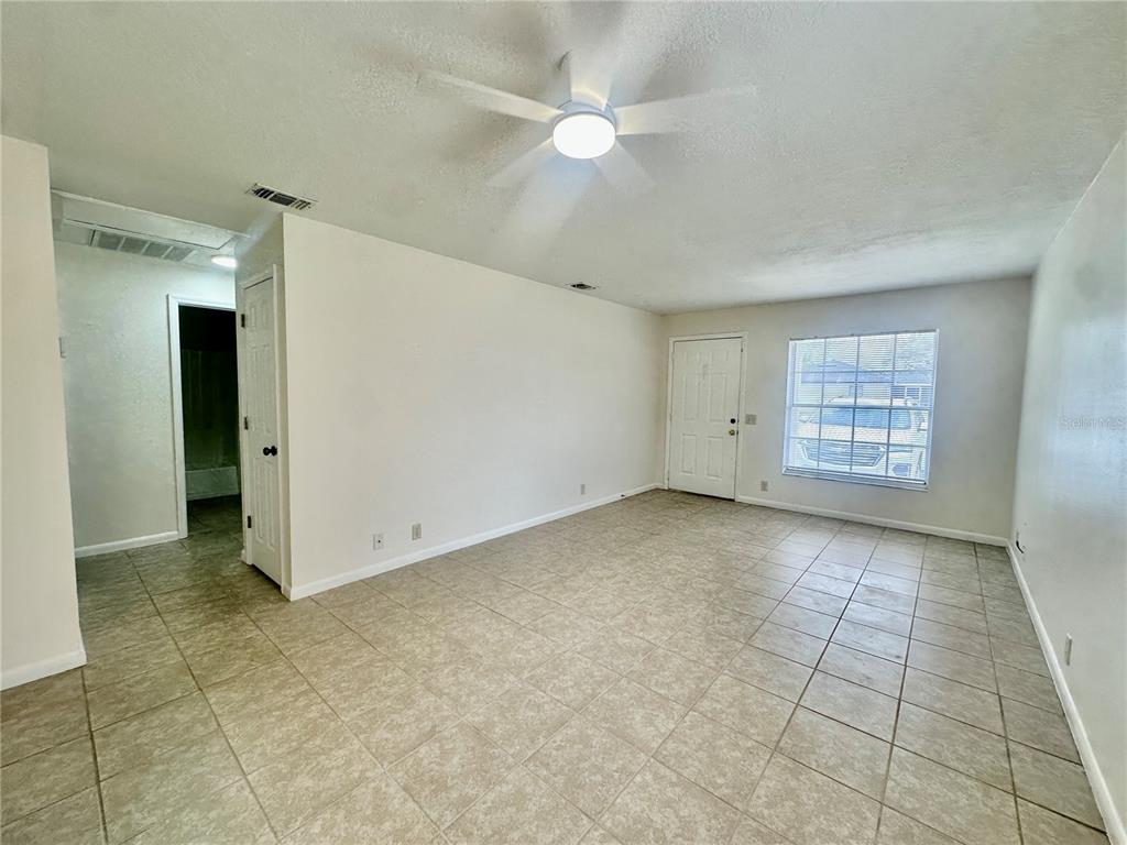 An empty living room features light-colored tile flooring, white walls, and a ceiling fan — 5638 STRUTHERS COURT, WINTER HAVEN, FL