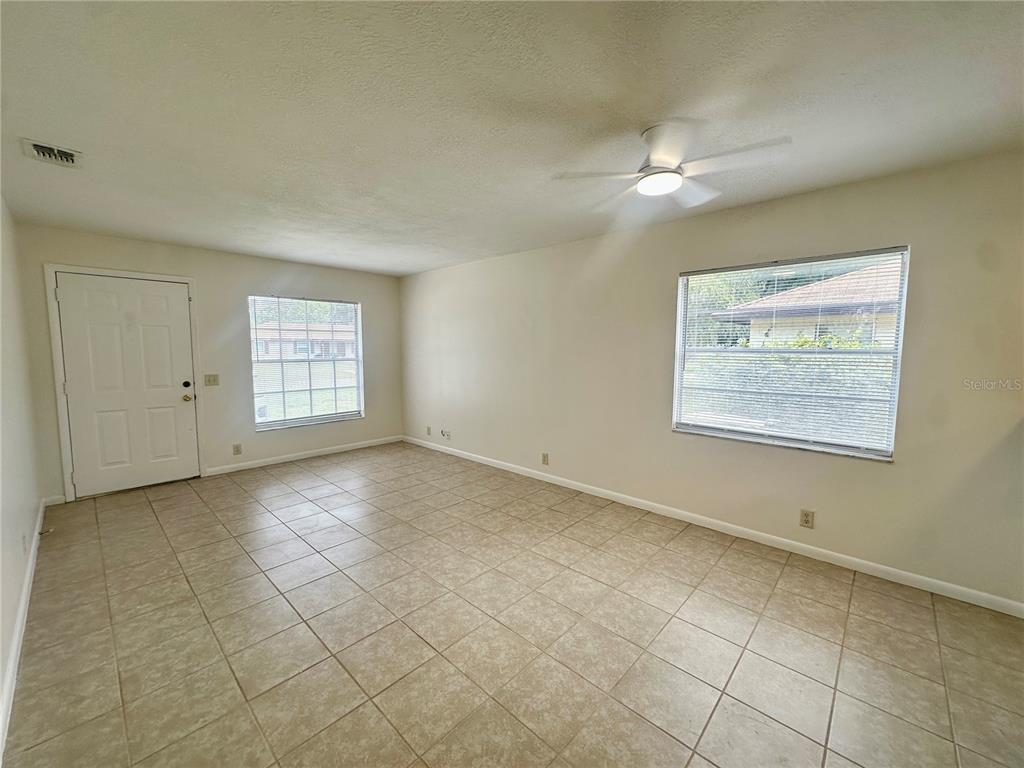 An empty room features beige tile flooring, white walls, a ceiling fan, and two windows — 5638 STRUTHERS COURT, WINTER HAVEN, FL
