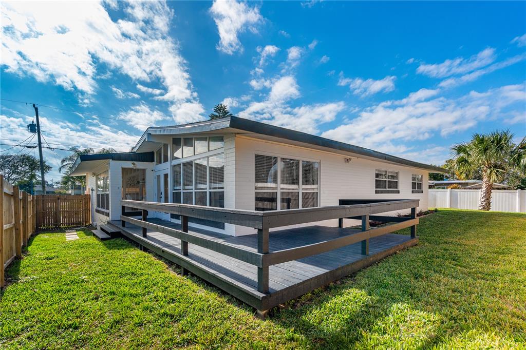 A white house with a dark wooden deck in a grassy backyard under a blue sky — 109 STANDISH DRIVE, ORMOND BEACH, FL