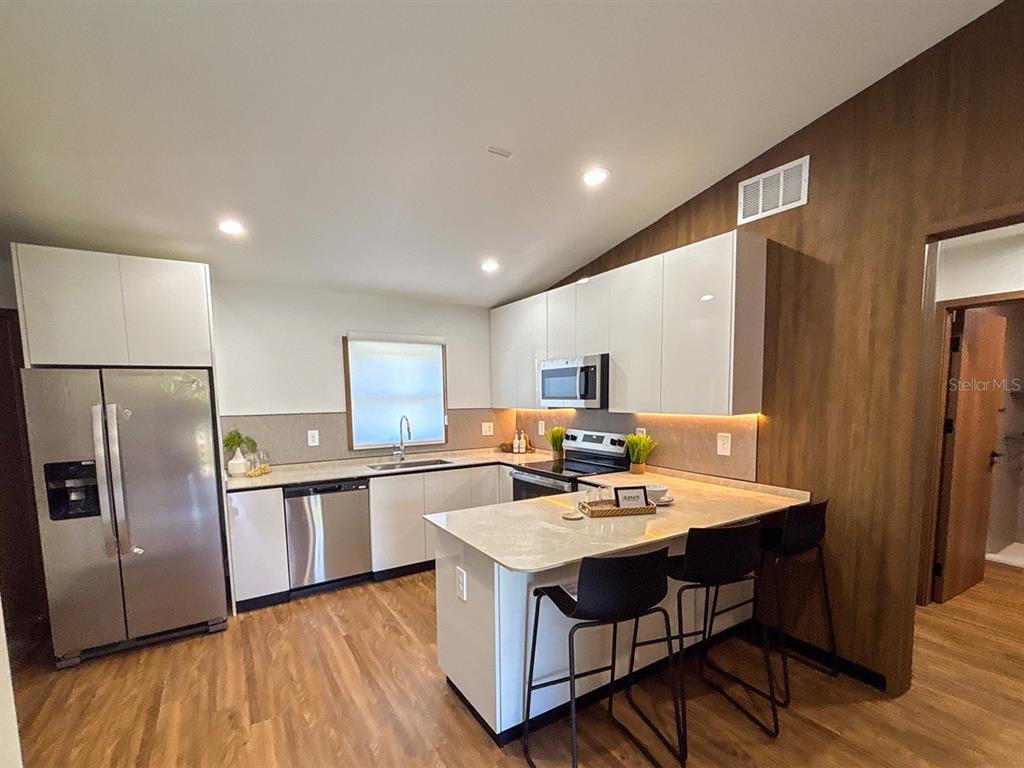 A modern kitchen features white cabinets, stainless steel appliances, and a breakfast bar with stools — 5620 VIRTUDES STREET, SEBRING, FL