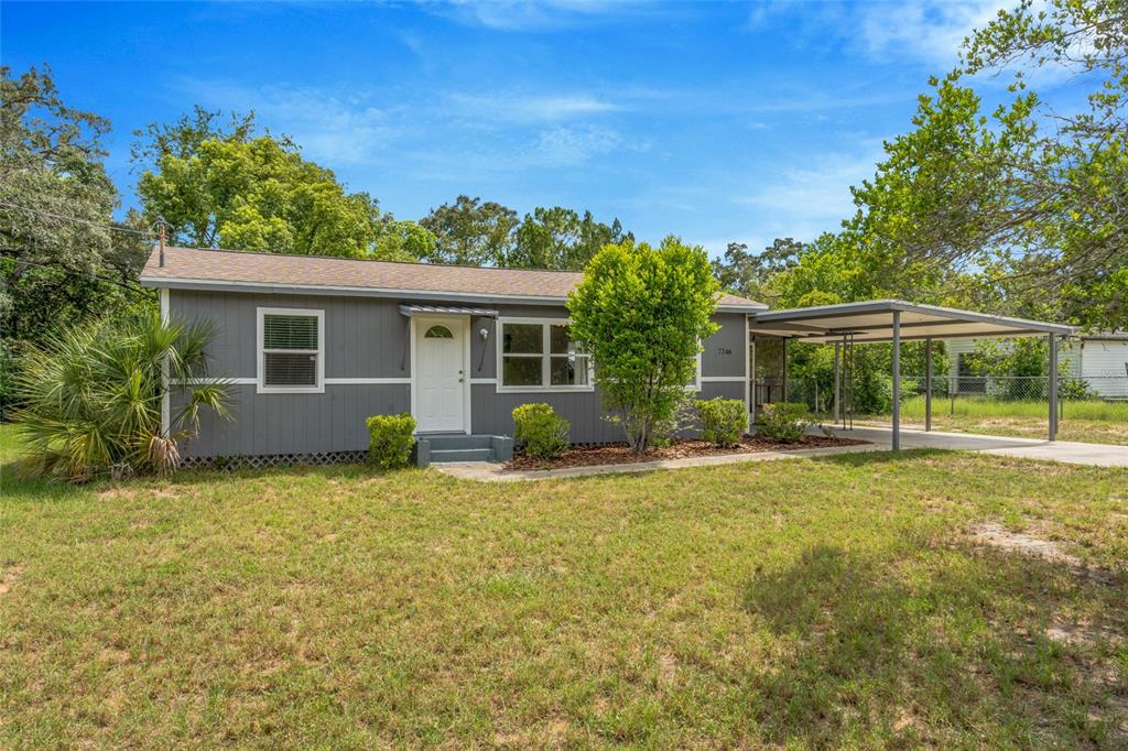 A gray single-story house features a concrete driveway, a covered carport, and a screened-in porch — 7246 SEALAWN DRIVE, SPRING HILL, FL