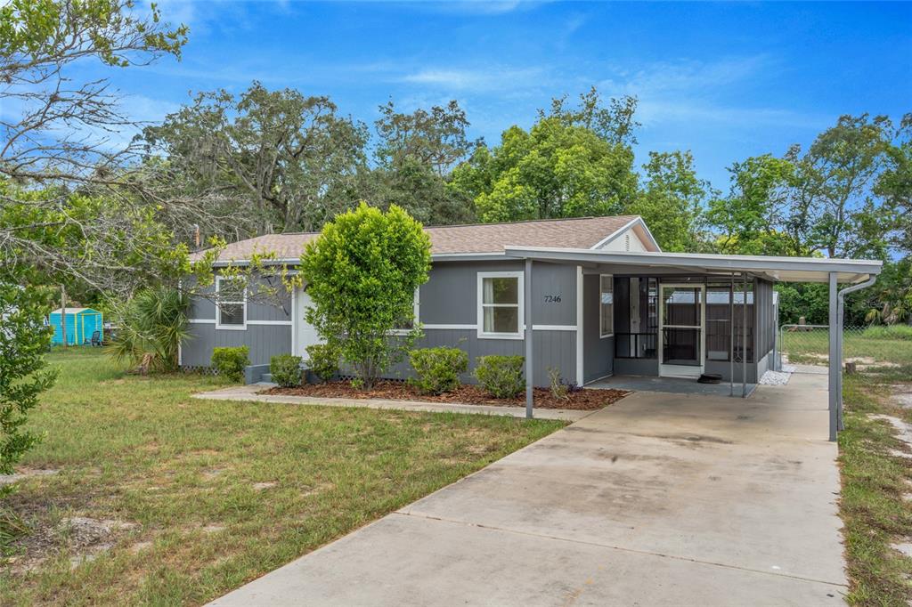 A gray single-story house features a concrete driveway, a covered carport, and a screened-in porch — 7246 SEALAWN DRIVE, SPRING HILL, FL