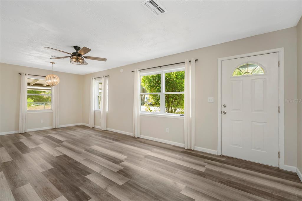 A living room with light-colored walls, wood-look flooring, a ceiling fan, and a front door — 7246 SEALAWN DRIVE, SPRING HILL, FL