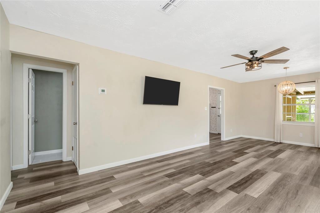 A living room with light walls, wood-look flooring, a ceiling fan, and a wall-mounted television — 7246 SEALAWN DRIVE, SPRING HILL, FL