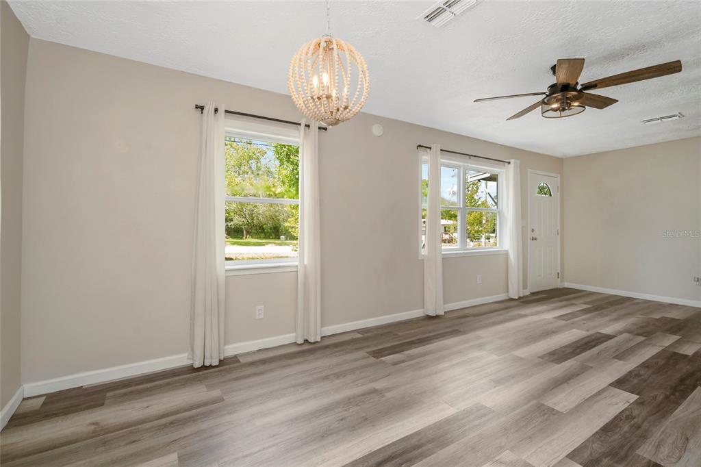 A bright living room features light-colored walls, wood-look flooring, a beaded chandelier, and a ceiling fan — 7246 SEALAWN DRIVE, SPRING HILL, FL