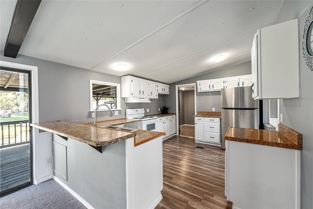 A kitchen features white cabinets, stainless steel appliances, granite-look countertops, and wood-look flooring — 5600 SE 39TH STREET, TRENTON, FL