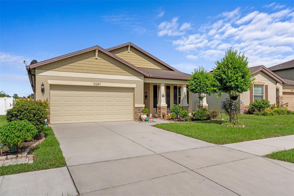A single-story suburban house with a tan exterior, two-car garage, and a front lawn — 15287 STONE HOUSE DRIVE, BROOKSVILLE, FL