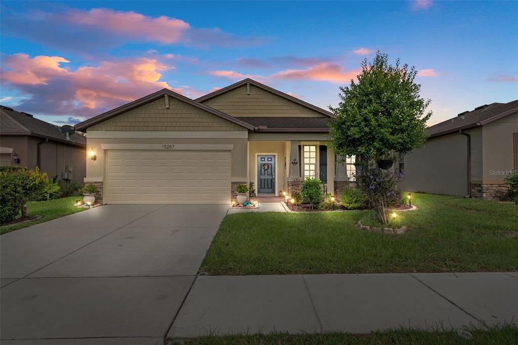 A single-story suburban house features a two-car garage, tan siding, and a covered front porch — 15287 STONE HOUSE DRIVE, BROOKSVILLE, FL