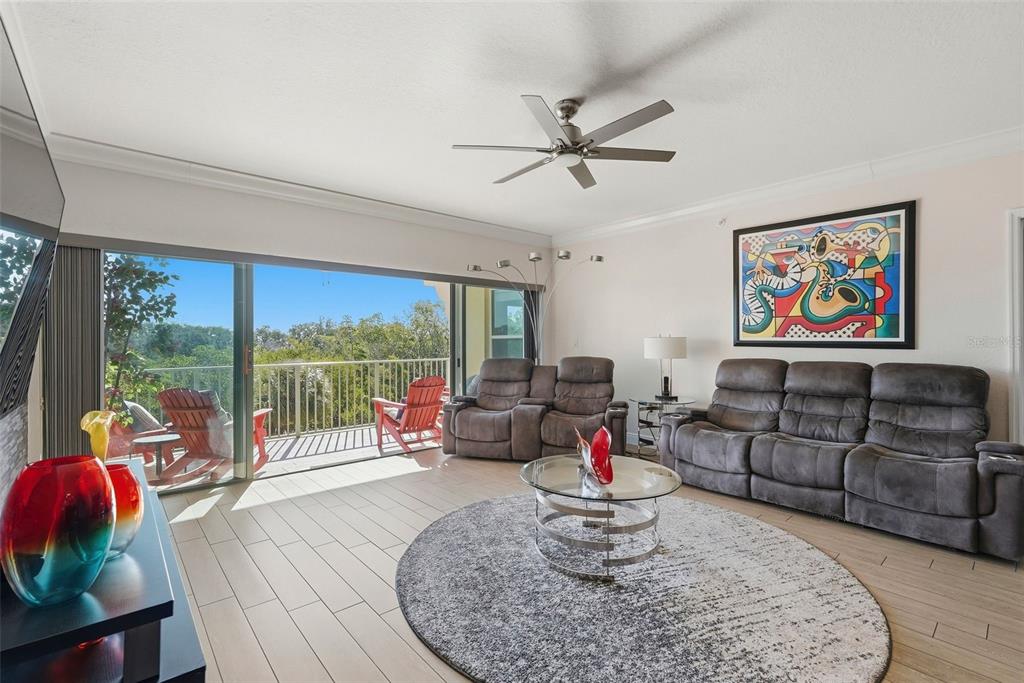 A living room features gray reclining sofas, a round rug, and a balcony with outdoor chairs — 1695 PINELLAS BAYWAY S UNIT E4, TIERRA VERDE, FL