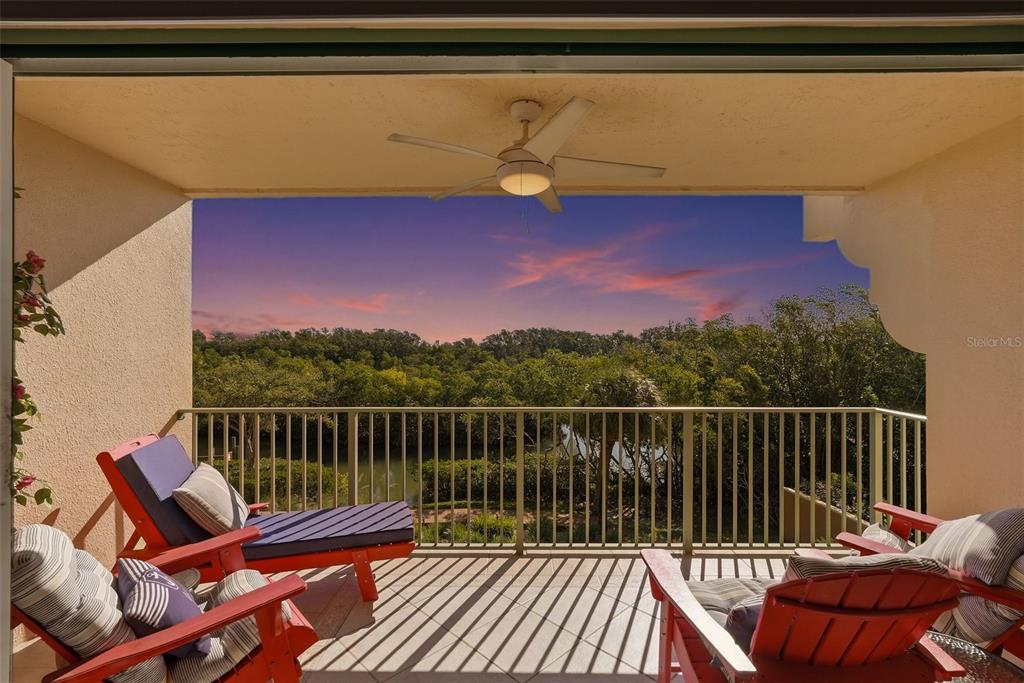 A covered balcony features red lounge chairs, a ceiling fan, and a view of trees — 1695 PINELLAS BAYWAY S UNIT E4, TIERRA VERDE, FL