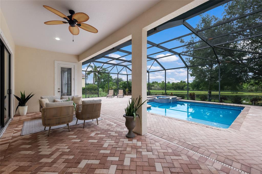 A covered patio with a pool, spa, and screened enclosure overlooking a grassy field — 12710 STONE RIDGE PLACE, BRADENTON, FL