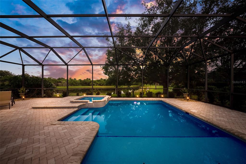 A swimming pool and spa are enclosed by a screened lanai overlooking a pond at sunset — 12710 STONE RIDGE PLACE, BRADENTON, FL