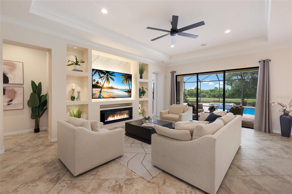 A living room features a fireplace, built-in shelving, a ceiling fan, and sliding glass doors — 12710 STONE RIDGE PLACE, BRADENTON, FL