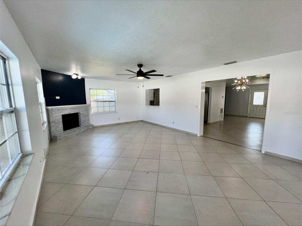 A spacious living room features light tile floors, a brick fireplace, and a ceiling fan — 1211 LEHIGH STREET, KISSIMMEE, FL