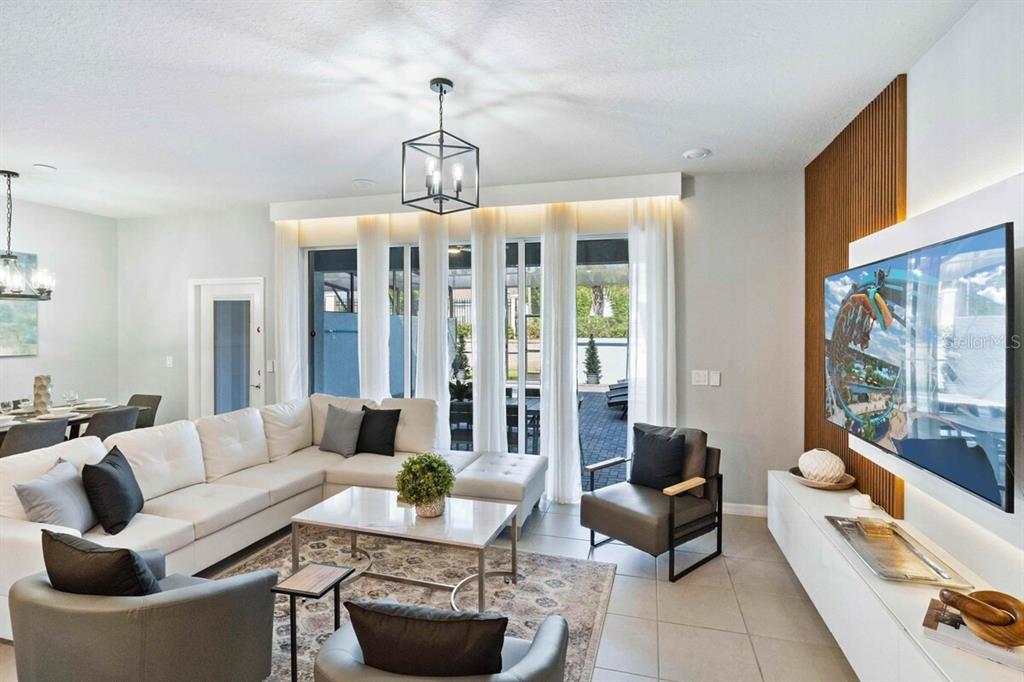 A modern living room features a white sectional sofa, a television, and floor-to-ceiling curtains — 107 JETTY WAY, DAVENPORT, FL