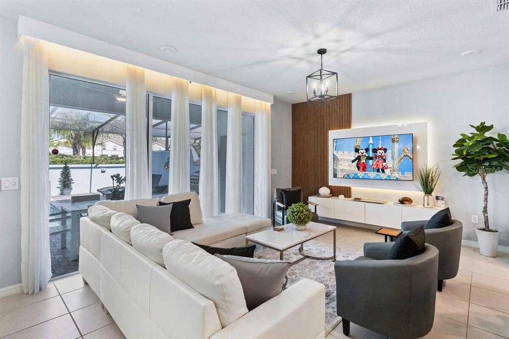 A modern living room features a white sectional, two gray armchairs, and a wall-mounted television — 107 JETTY WAY, DAVENPORT, FL
